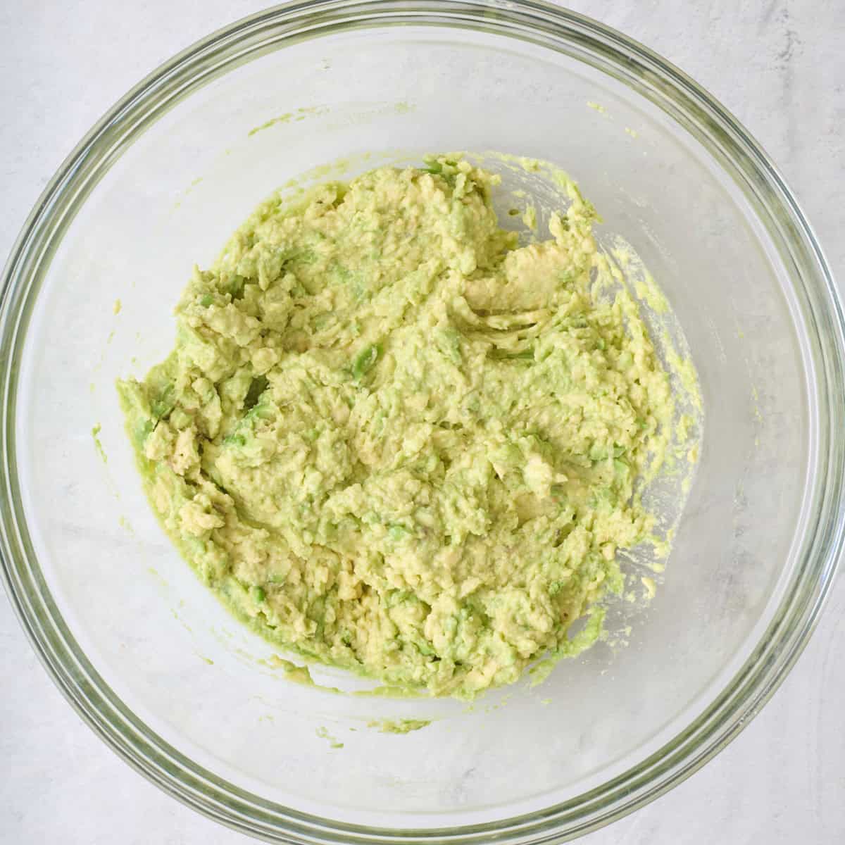 Mashed avocados in a large glass mixing bowl.