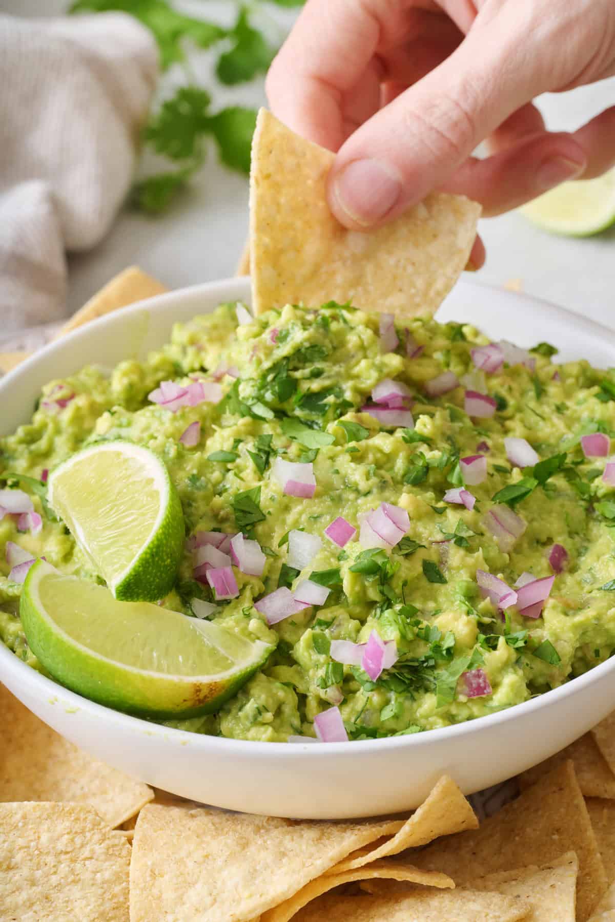 A tortilla chip being used to scoop up guacamole from a bowl.