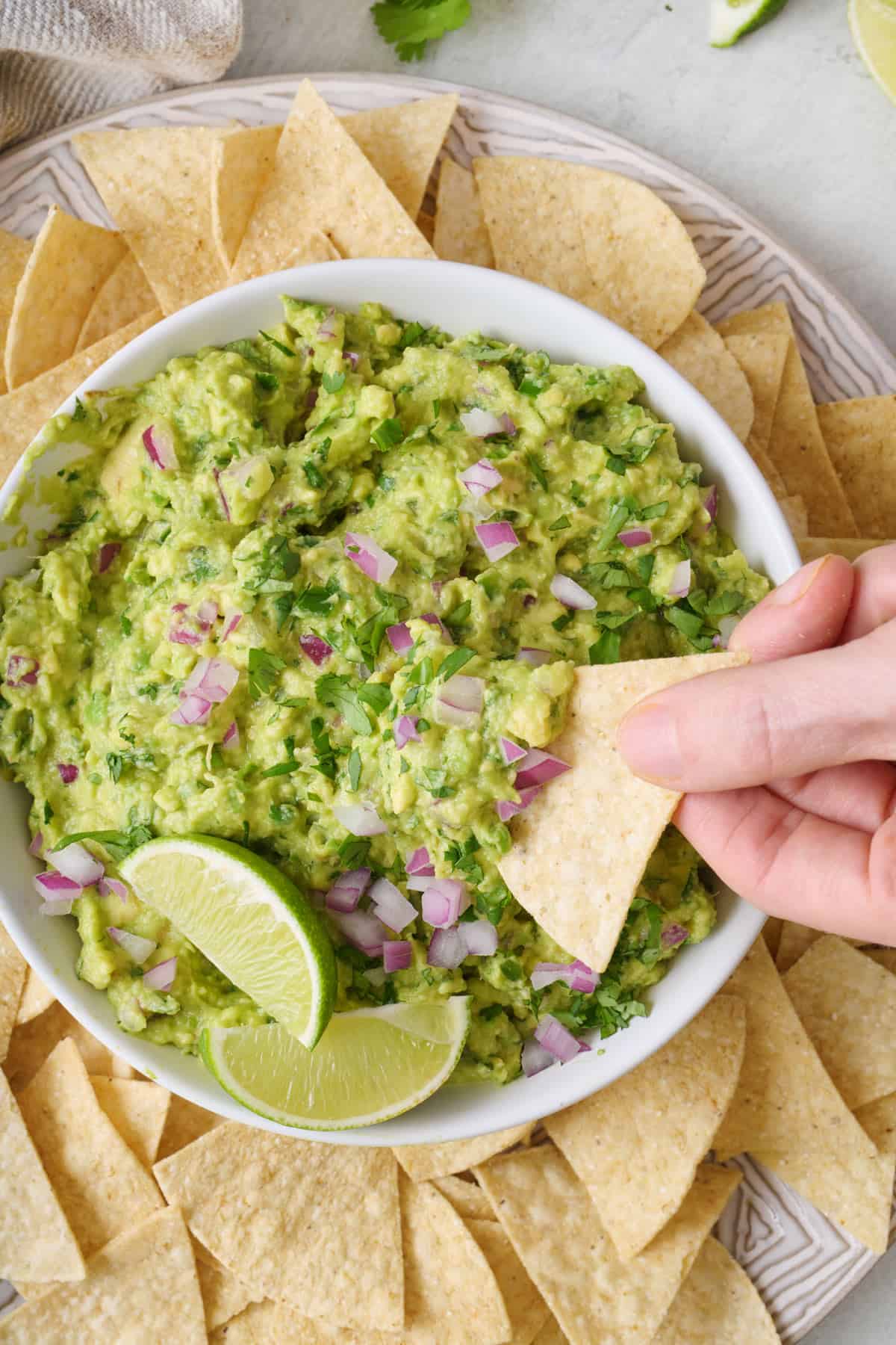 A person using a tortilla chip to scoop up guacamole out of a bowl.