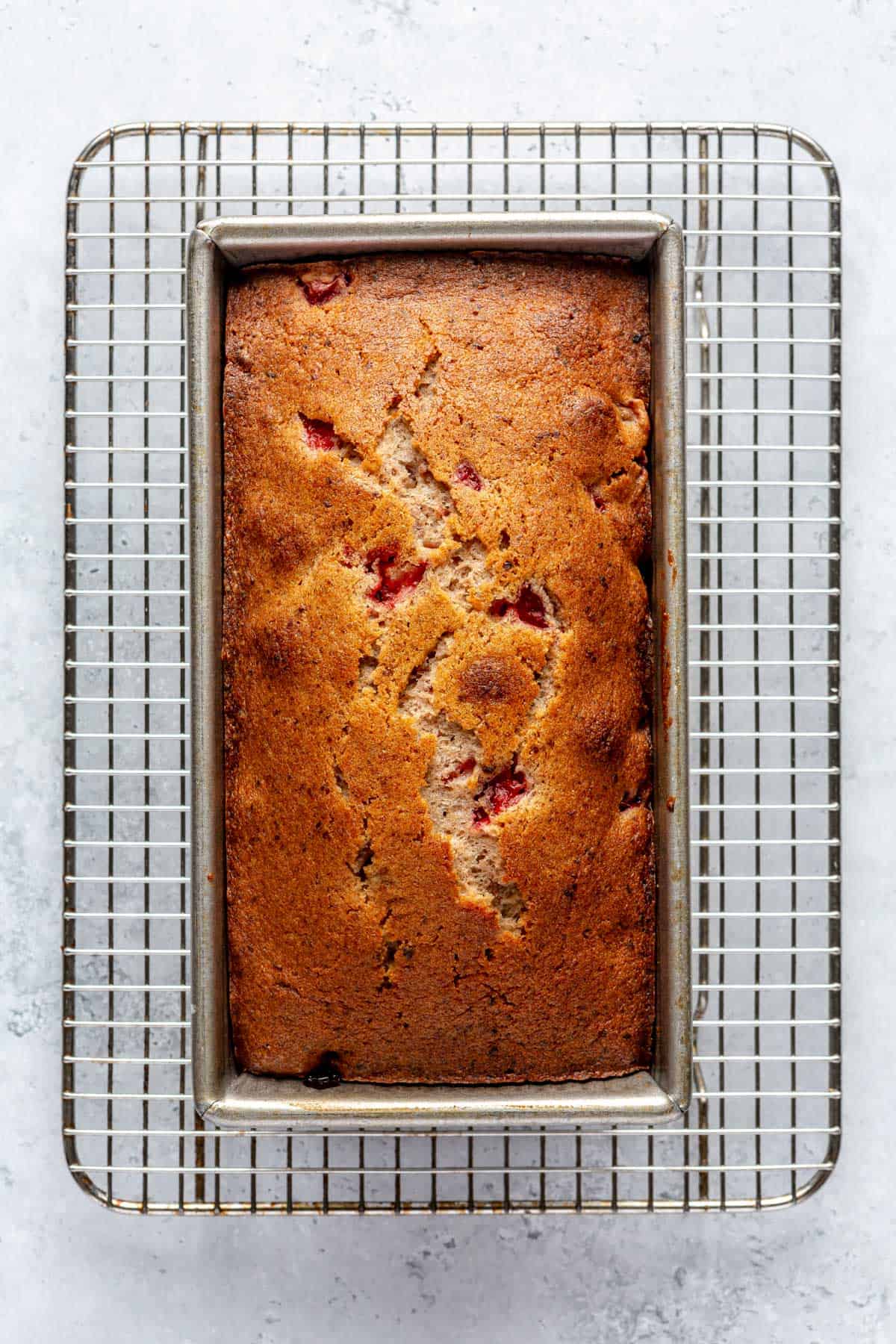 A baked strawberry pound cake in a loaf pan on a cooling rack.