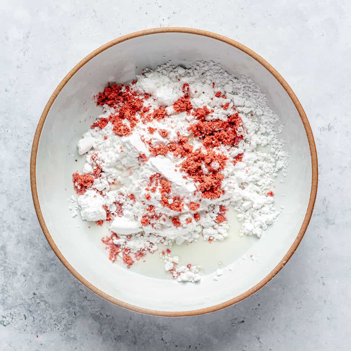 Powdered sugar, freeze-dried strawberry powder, and milk in a small bowl.