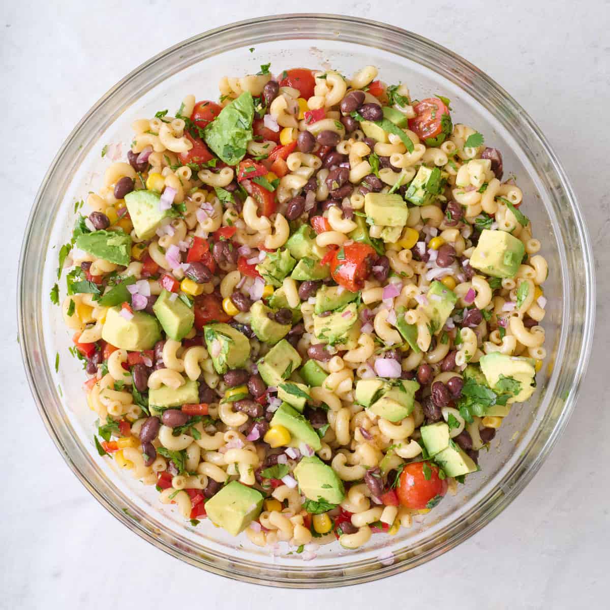 Taco pasta salad topped with cubed avocado in a large glass mixing bowl.