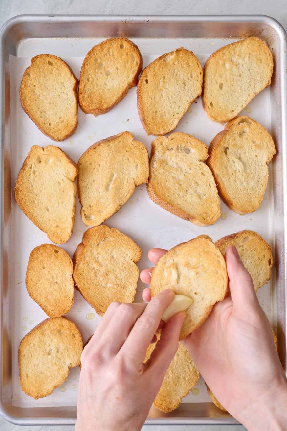 A person rubbing a garlic clove onto toasted bread.