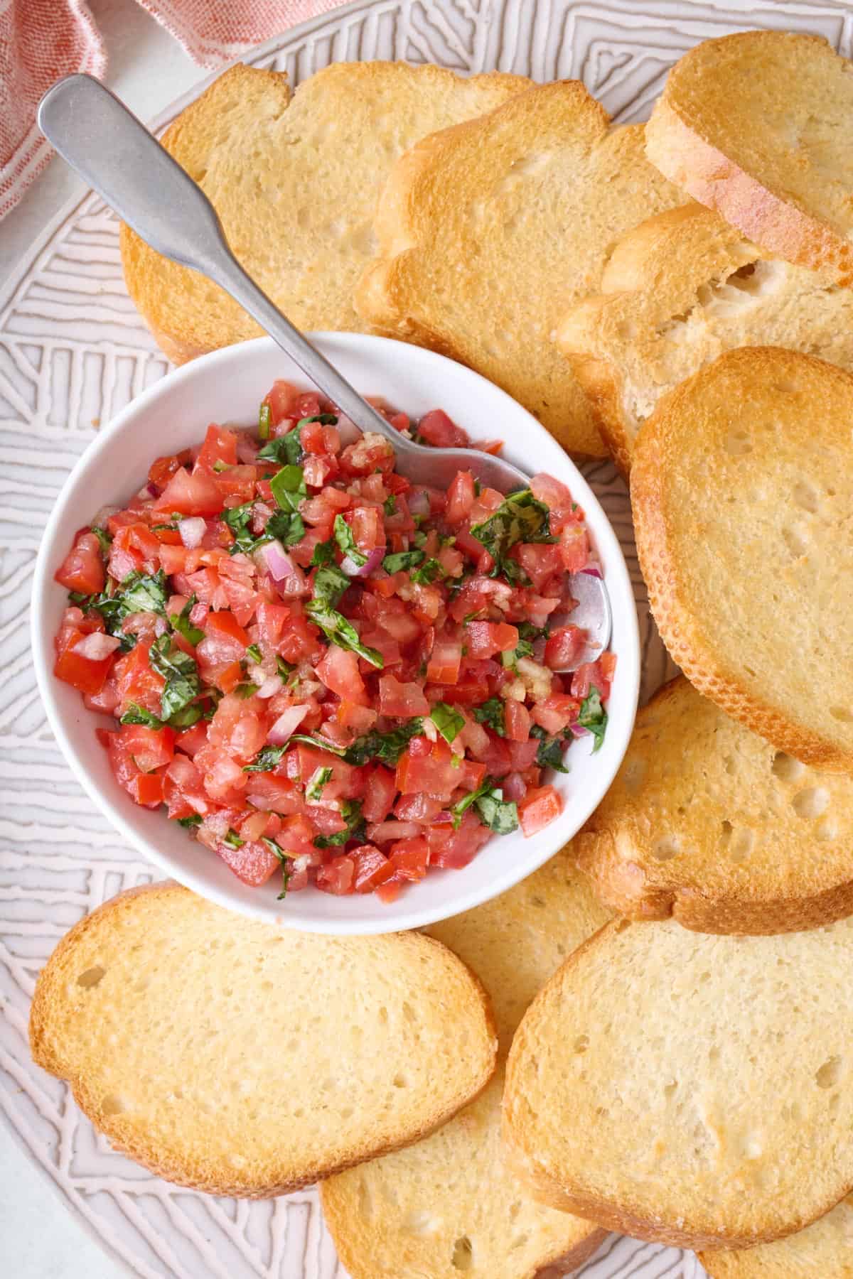 A bowl of tomato basil mixture beside pieces of toast.