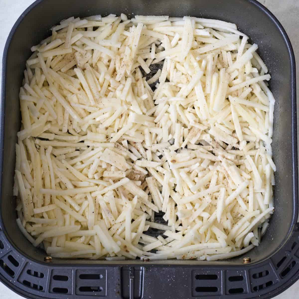 Frozen, shredded potatoes in an air fryer basket.