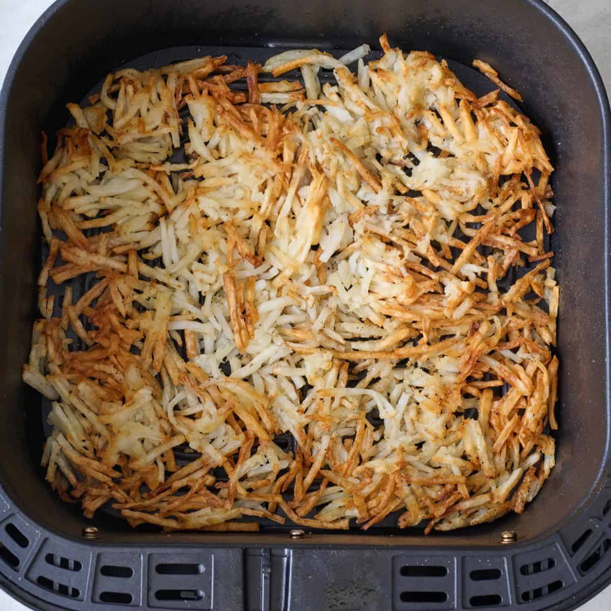 Crispy, shredded potatoes in an air fryer basket.