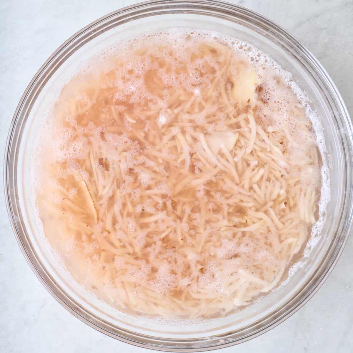 Shredded potatoes soaking in a bowl of water.