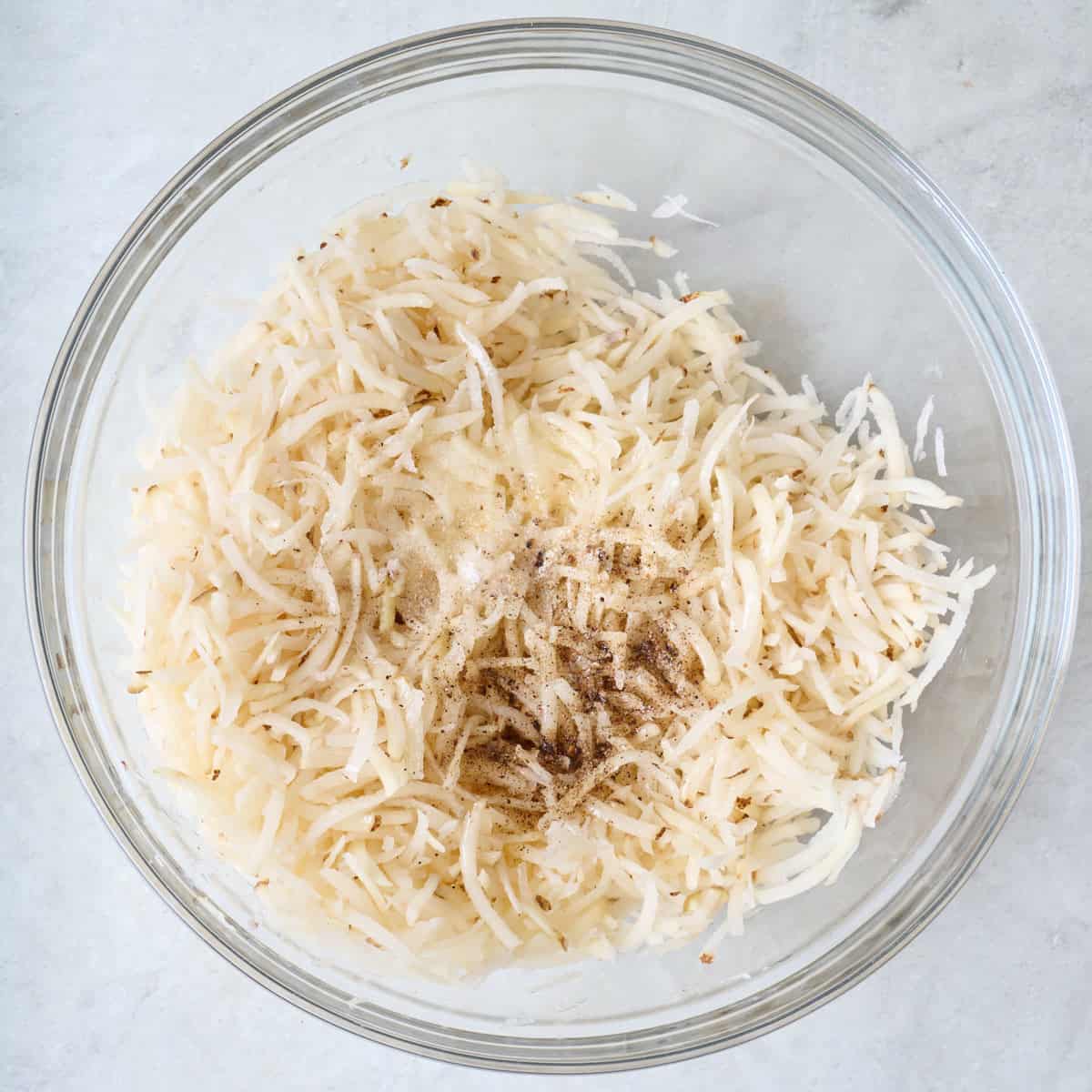 Shredded potatoes and spices in a mixing bowl.