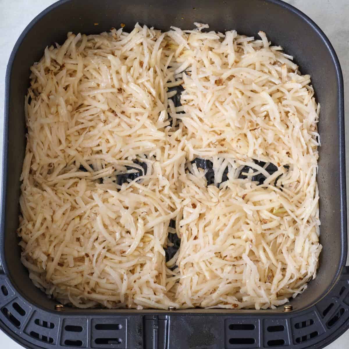 Shredded potatoes in an air fryer basket.