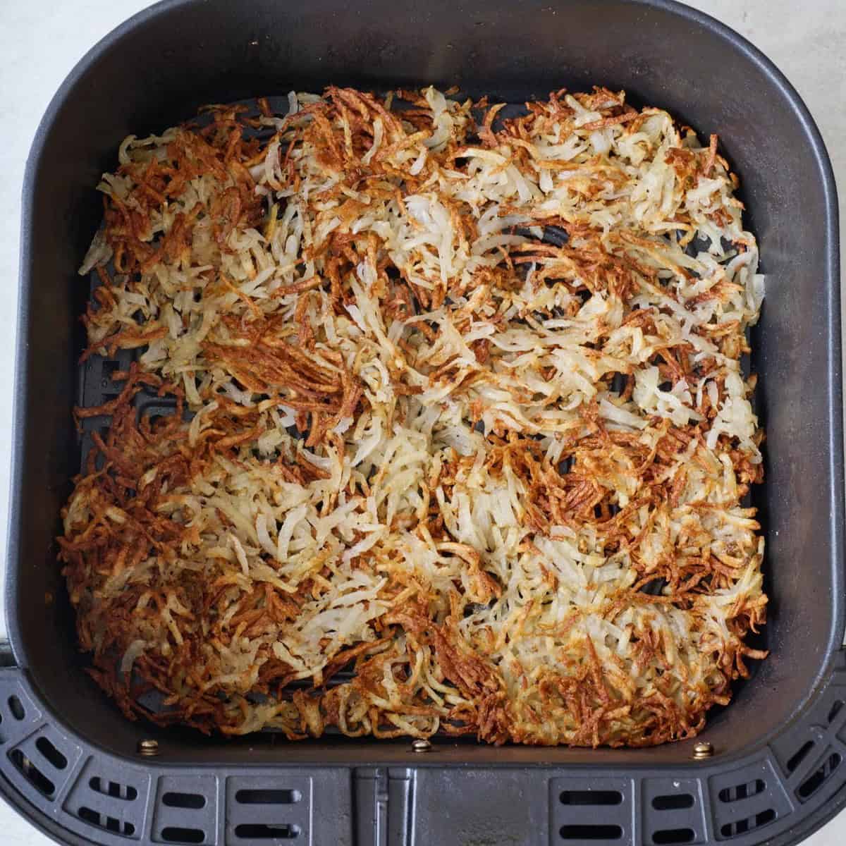 Cooked, crispy hash browns in an air fryer basket.