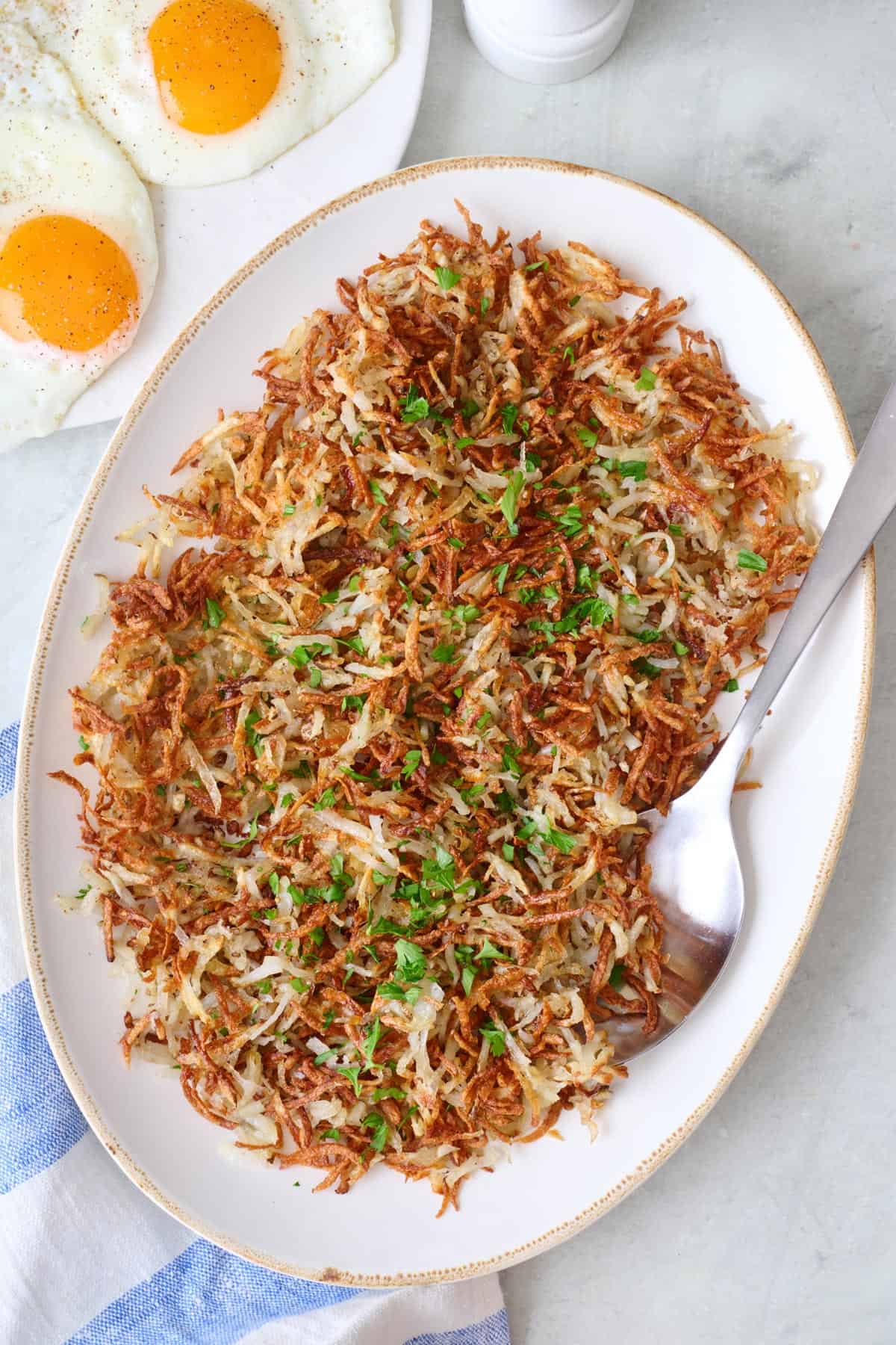 A platter with air fryer hash browns on it. A plate with fried eggs sits beside the platter.