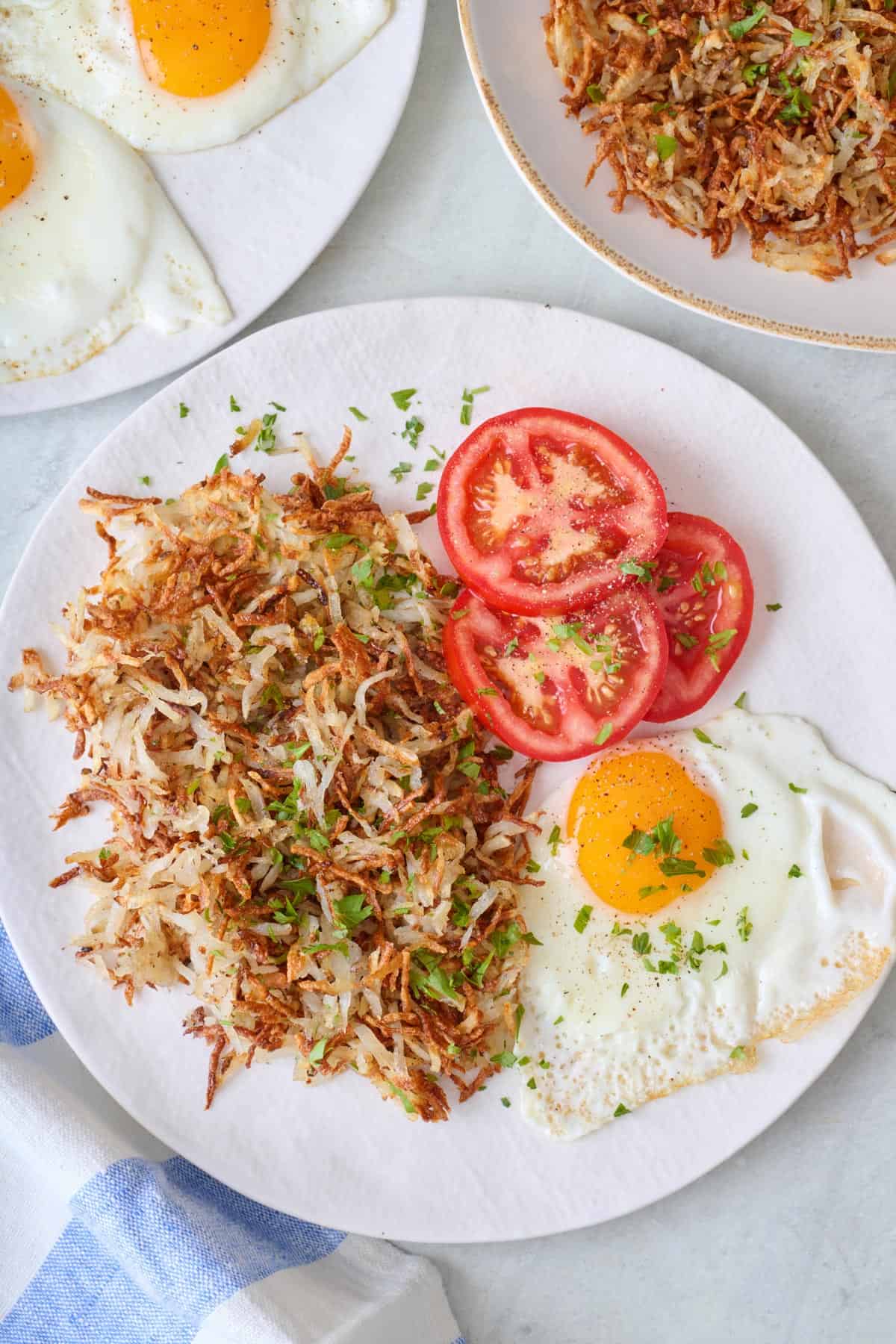 A plate with air fryer hash browns, sliced tomatoes, and a fried egg.