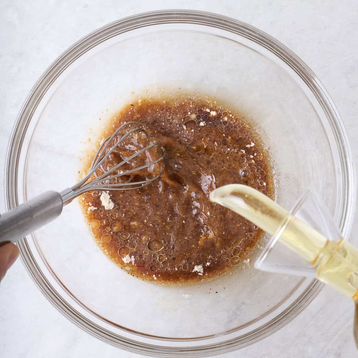 Emulsifying dressing with a whisk while pouring in oil.