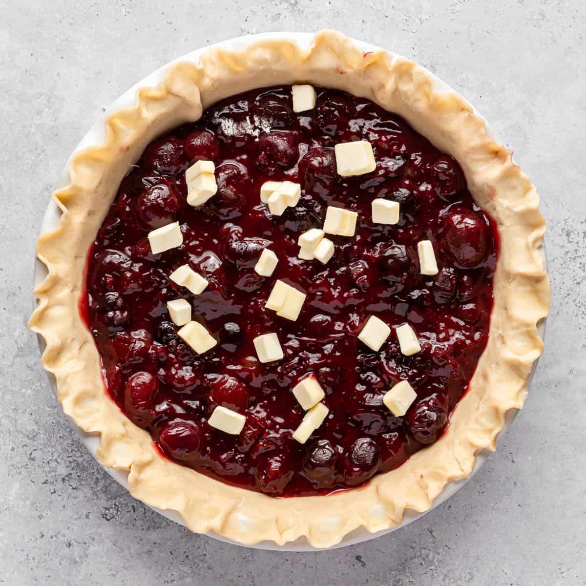 A pie crust in a pie plate filled with cherry pie filling.