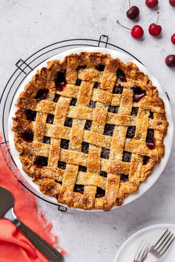 Homemade cherry pie with coarse sugar sprinkled over a lattice crust with fresh cherries nearby.