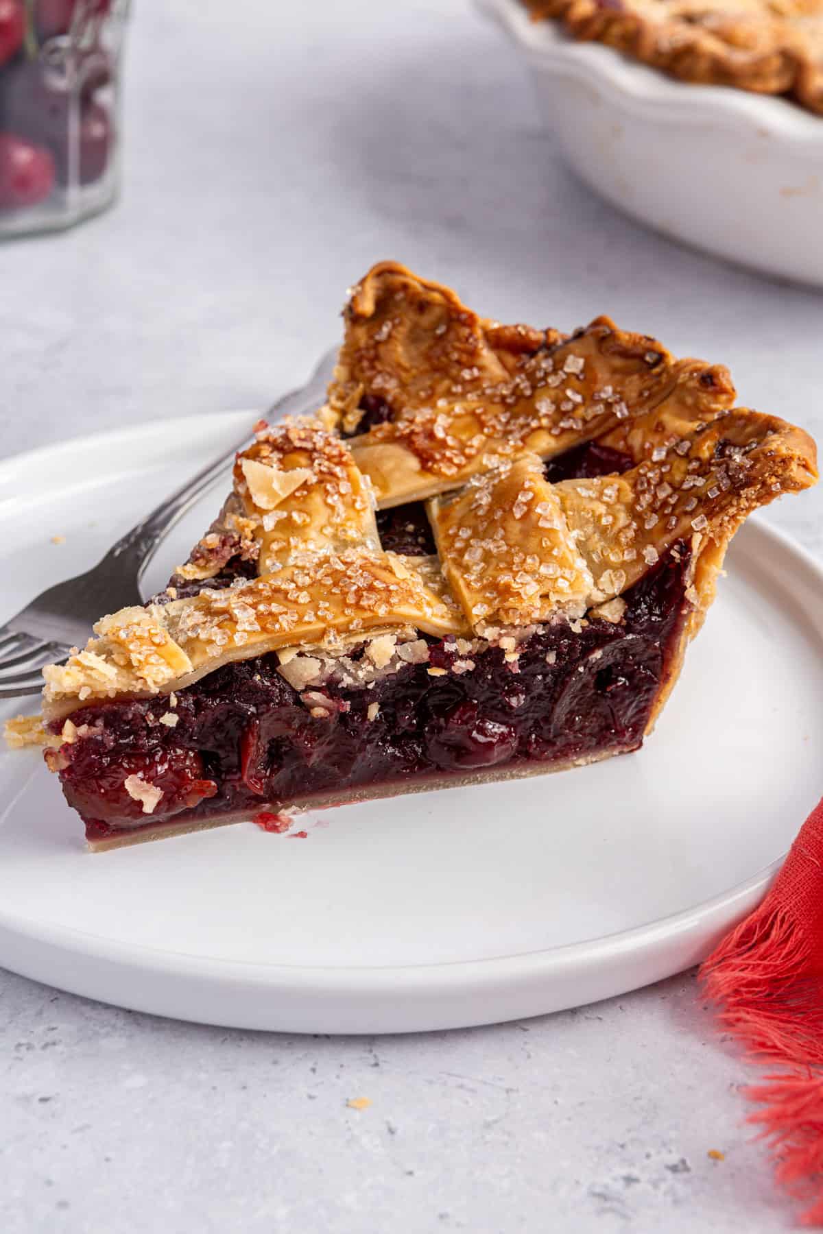 Slice of homemade cherry pie on a plate with a lattice pie crust.