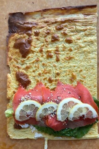 Cottage cheese flatbread on cutting board with cream cheese, salmon, lettuce, everything seasoning and lemon slices