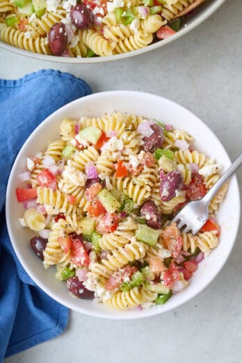 Greek pasta salad in a small bowl with a fork dipped inside.