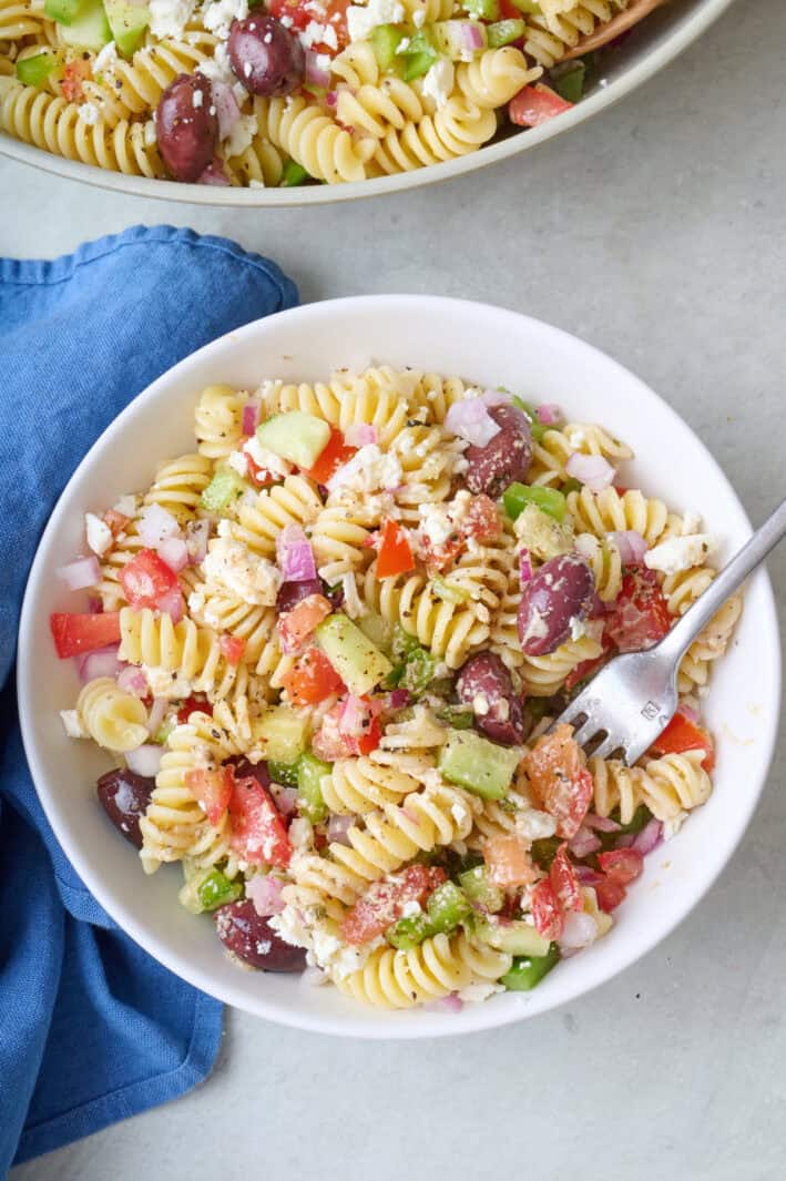 Greek pasta salad in a small bowl with a fork dipped inside.