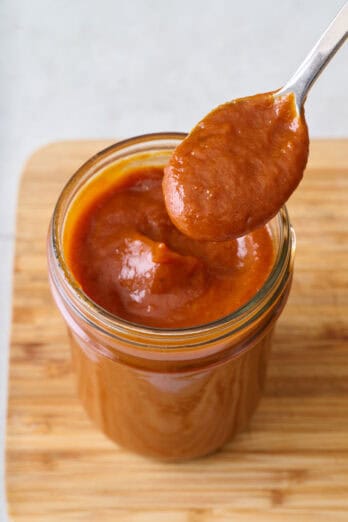 Spoon lifting bbq sauce from jar for tutorial on how to make bbq sauce.
