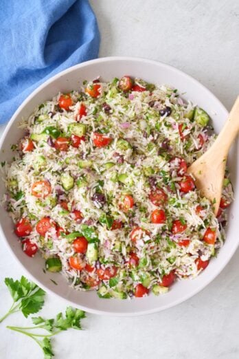 Mediterranean rice salad in a serving bowl with a wood serving spoon dipped inside.