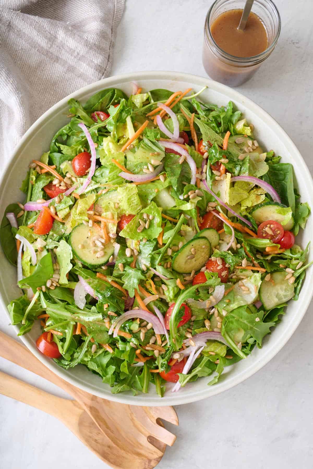 A mixed greens salad in a large white serving bowl.