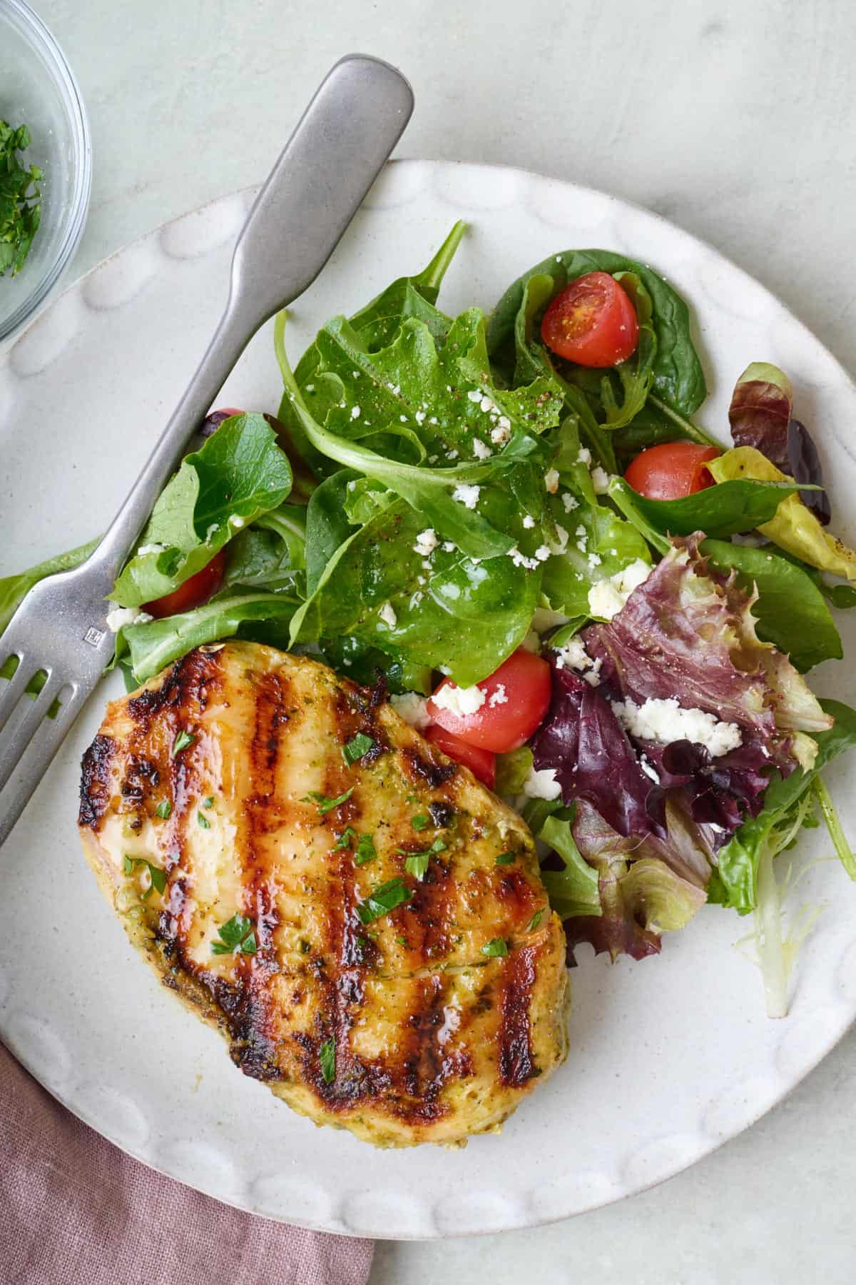 Pesto yogurt grilled chicken breast on a plate with a fresh spring salad.