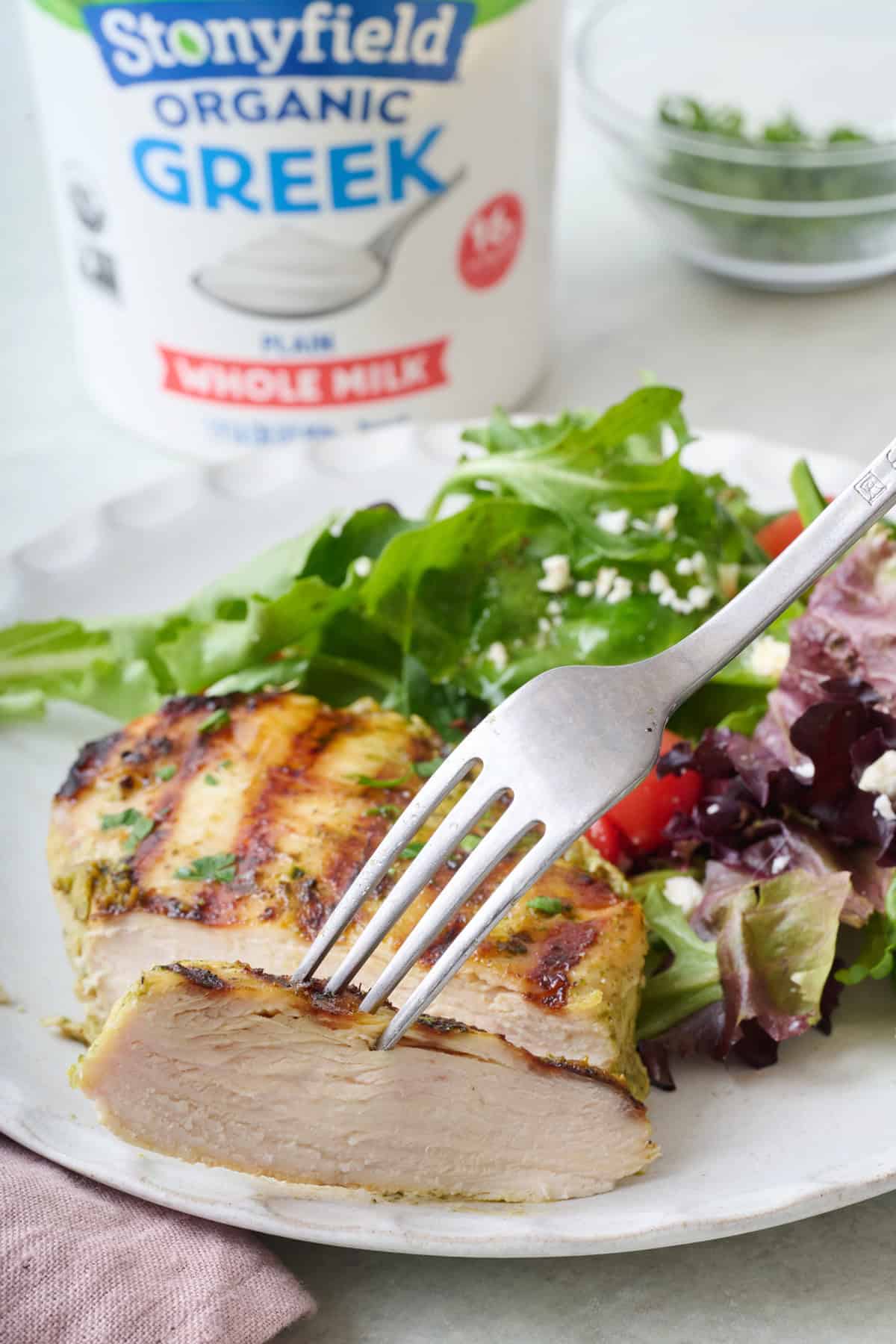 Stonyfield Organic Whole Milk Greek Yogurt and pesto marinated chicken breasts on a plate with a fork lifting up a cut piece.