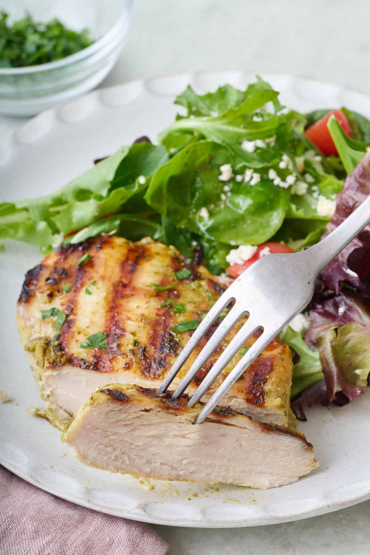 Grilled pesto chicken on a plate with a slice cut away and lifted by fork.