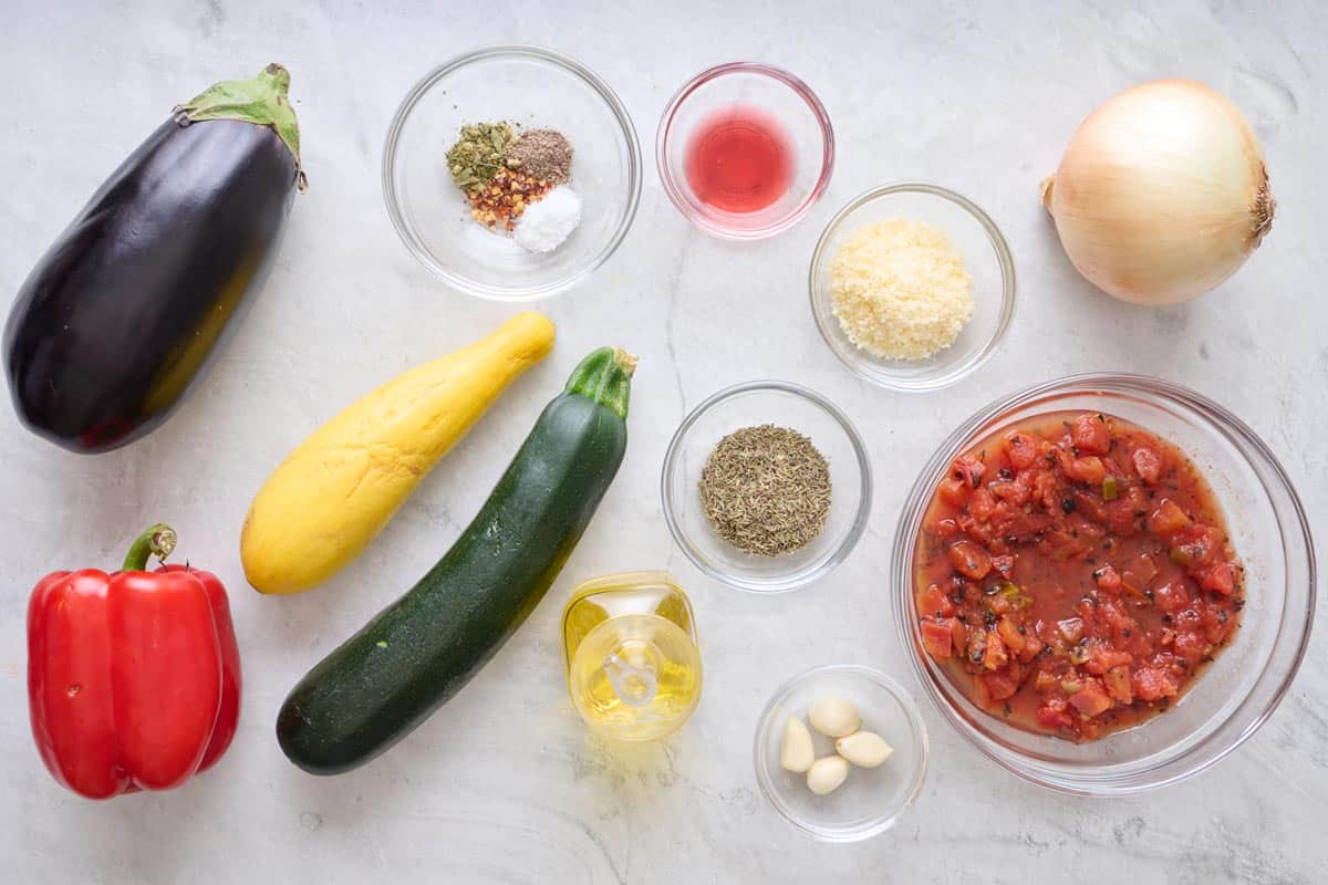Ingredients to make recipe: eggplant, red bell pepper, yellow squash, zucchini, seasoning blend, red wine vinegar, parmesan cheese, dried oregano, garlic cloves, fire roasted diced tomatoes, and an onion.