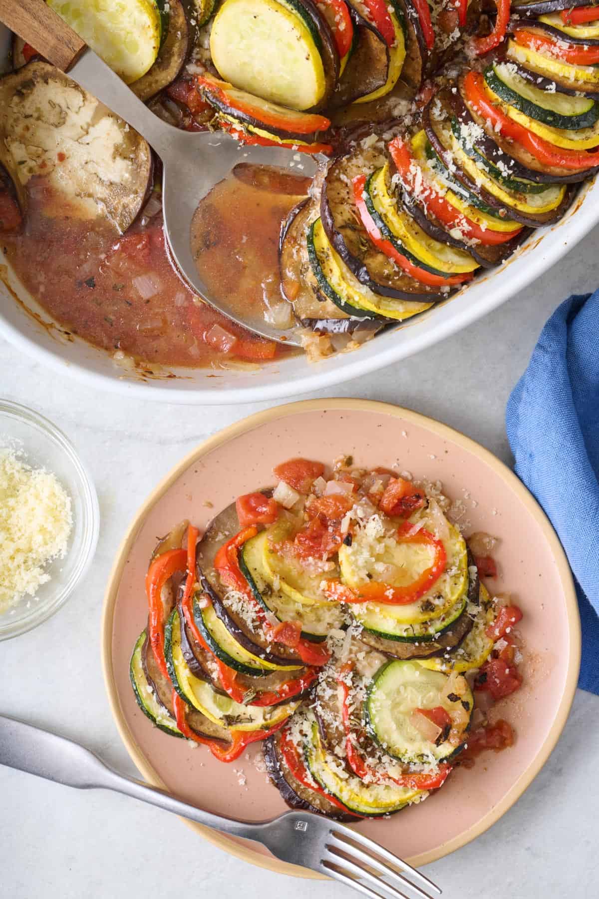 Baking dish of ratatouille with serving removed to a plate on the side to show tomato sauce mixture on the bottom of pan.