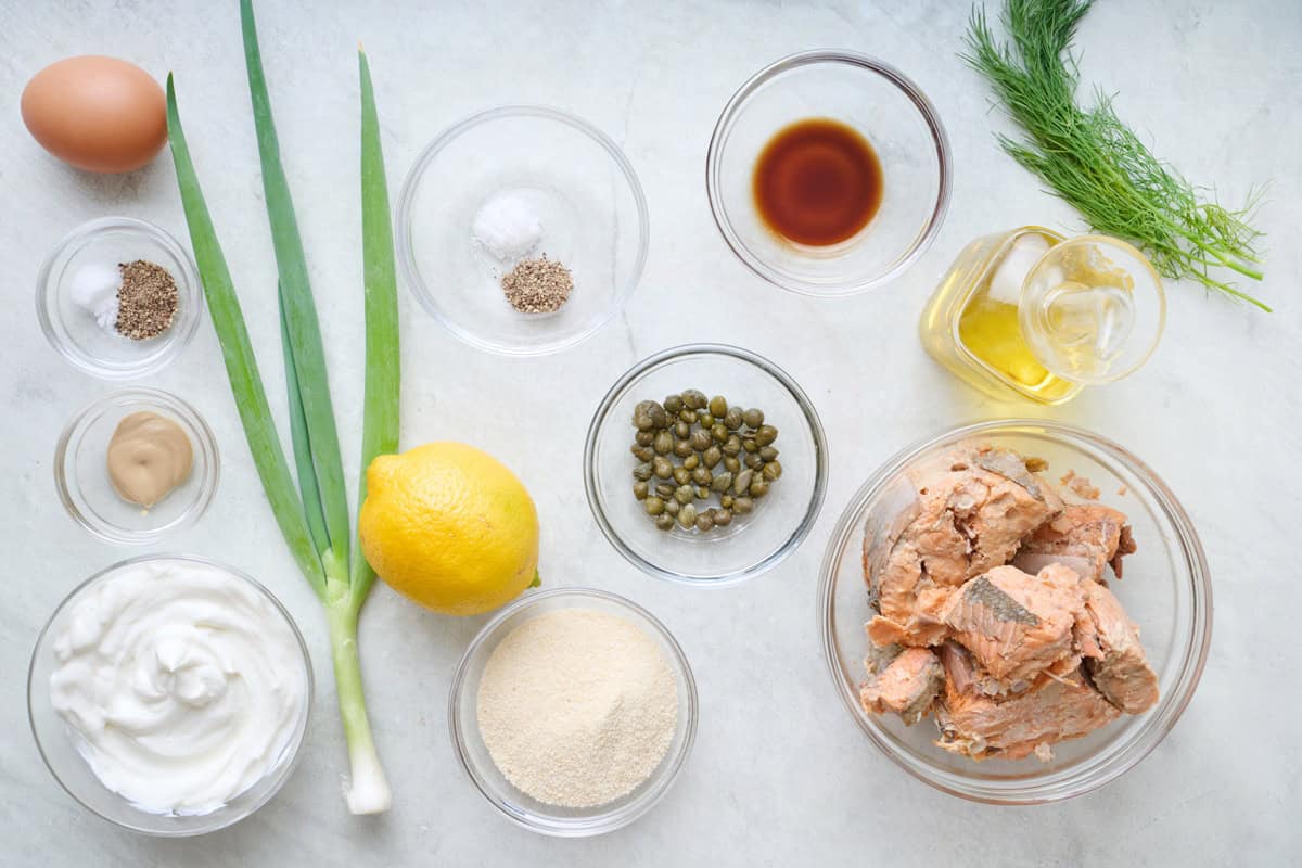 Ingredients for recipe: egg, salt and pepper, Dijon mustard, yogurt, green onions, capers, lemon, breadcrumbs, Worcestershire sauce, oil, canned salmon, and fresh dill.