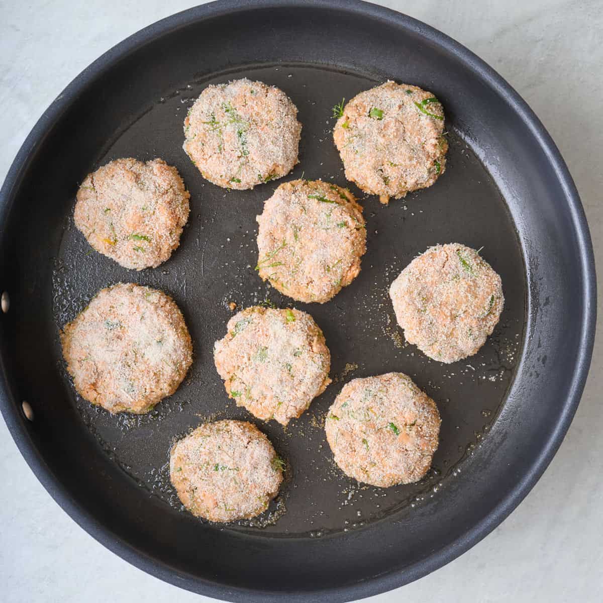 Breadcrumb coated salmon patties on an oiled skillet.