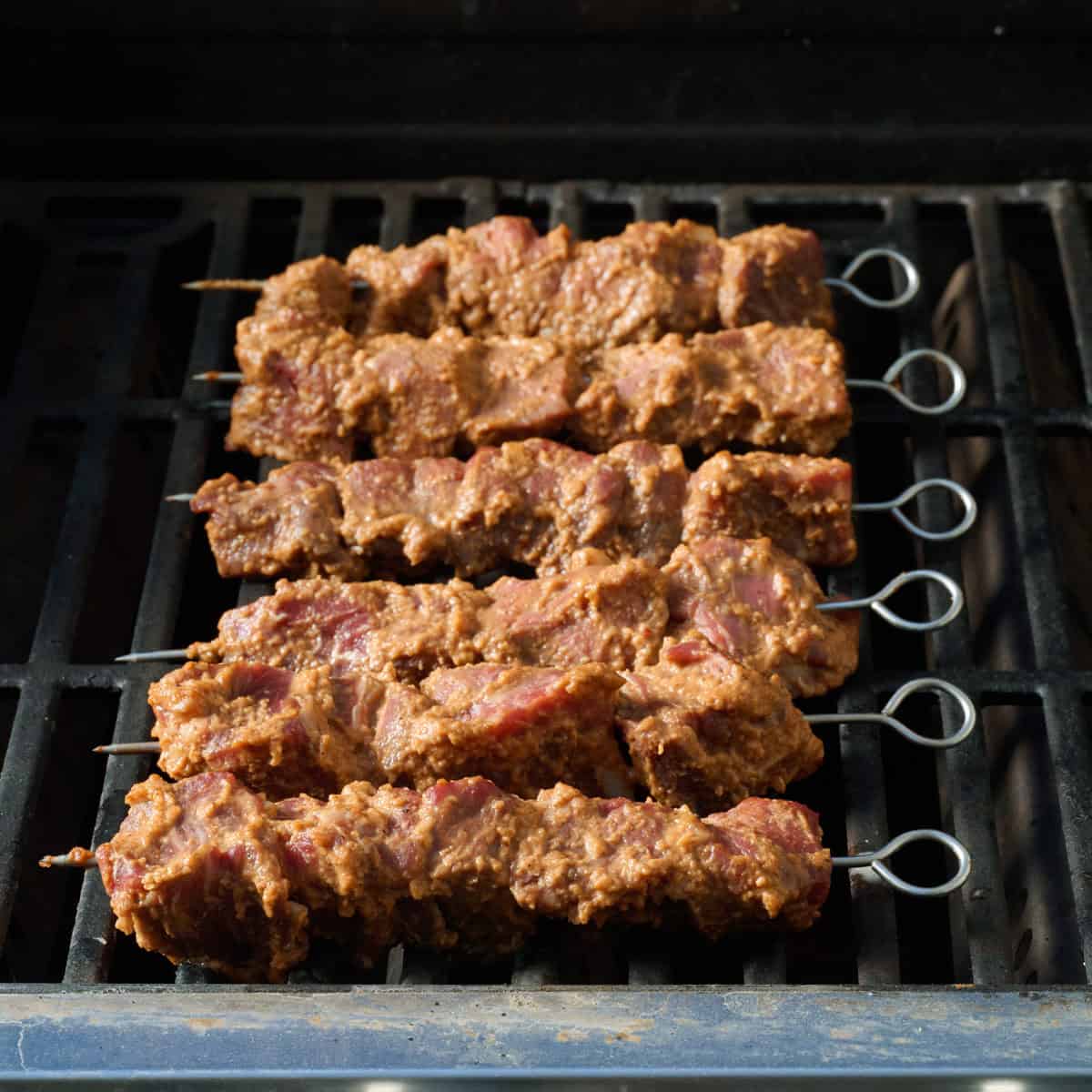 Skewered marinated beef on a grill before cooking.