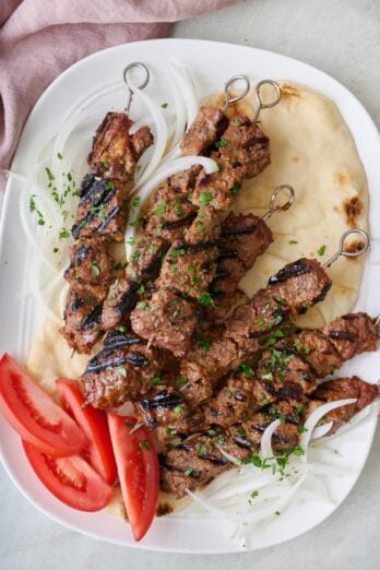 West African beef skewers on a large pita served on a platter with onions and tomatoes.