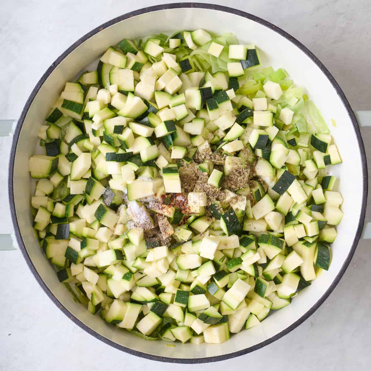 Cubed zucchini, leeks, and seasoning in a Dutch oven.