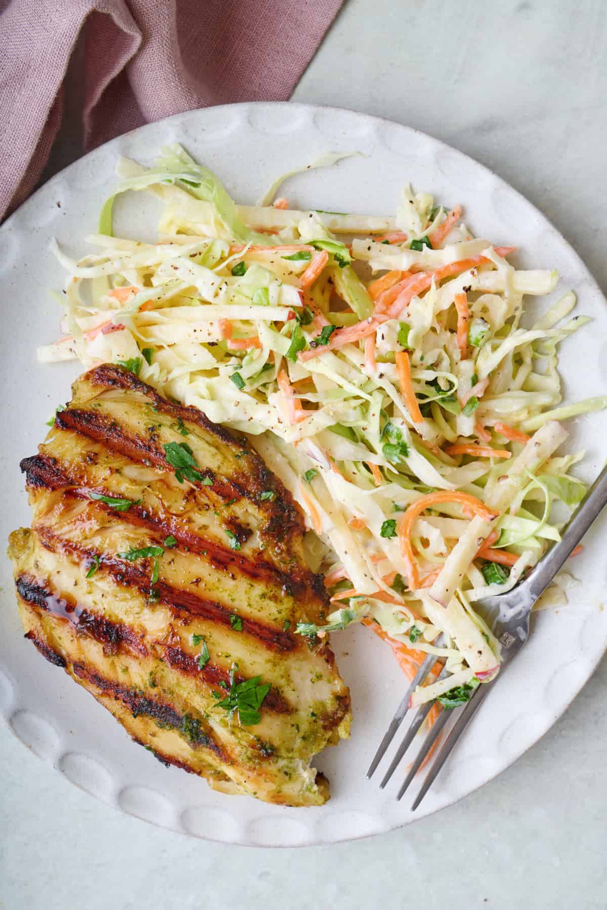 Serving of apple slaw on a place with grilled chicken.