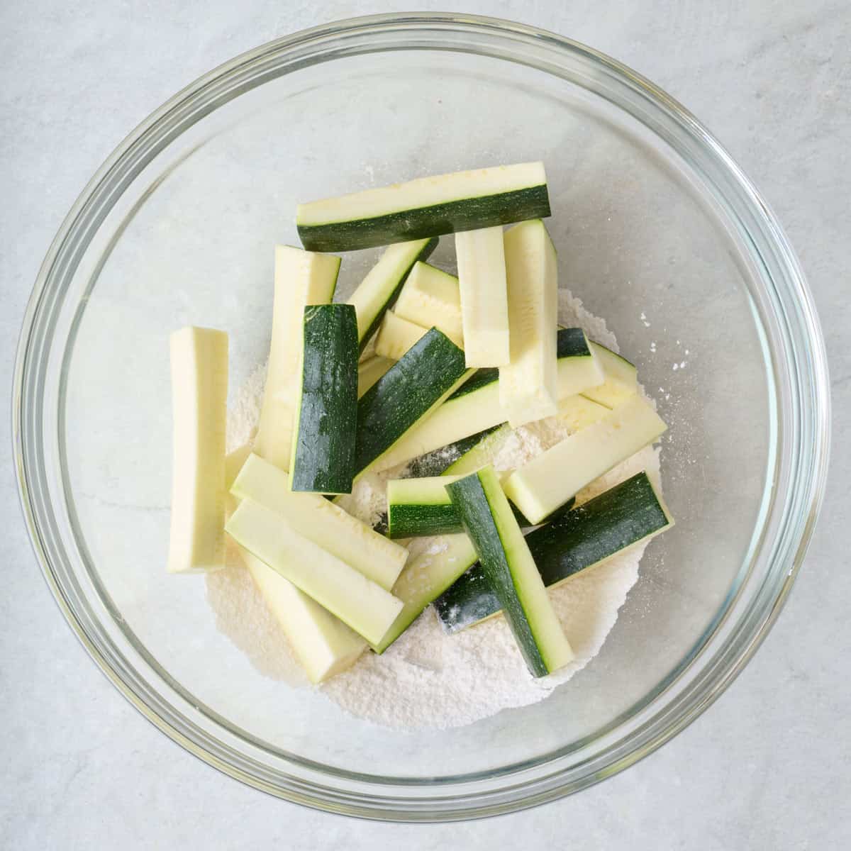 Zucchini sticks and flour in a large mixing bowl.