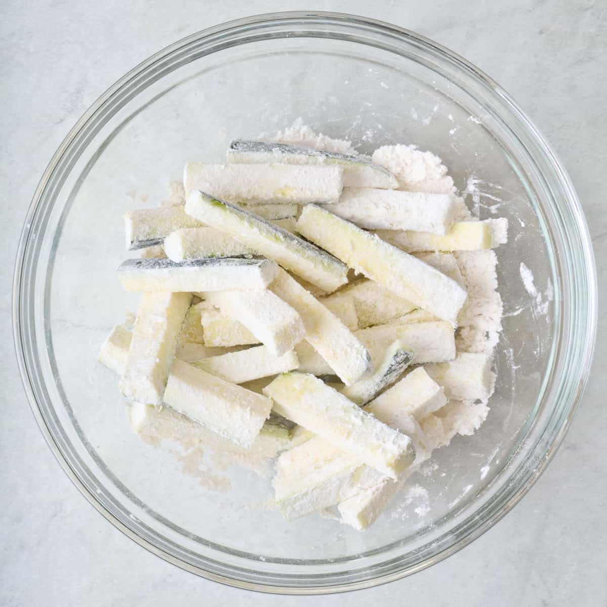 Zucchini sticks topped with flour in a large mixing bowl.