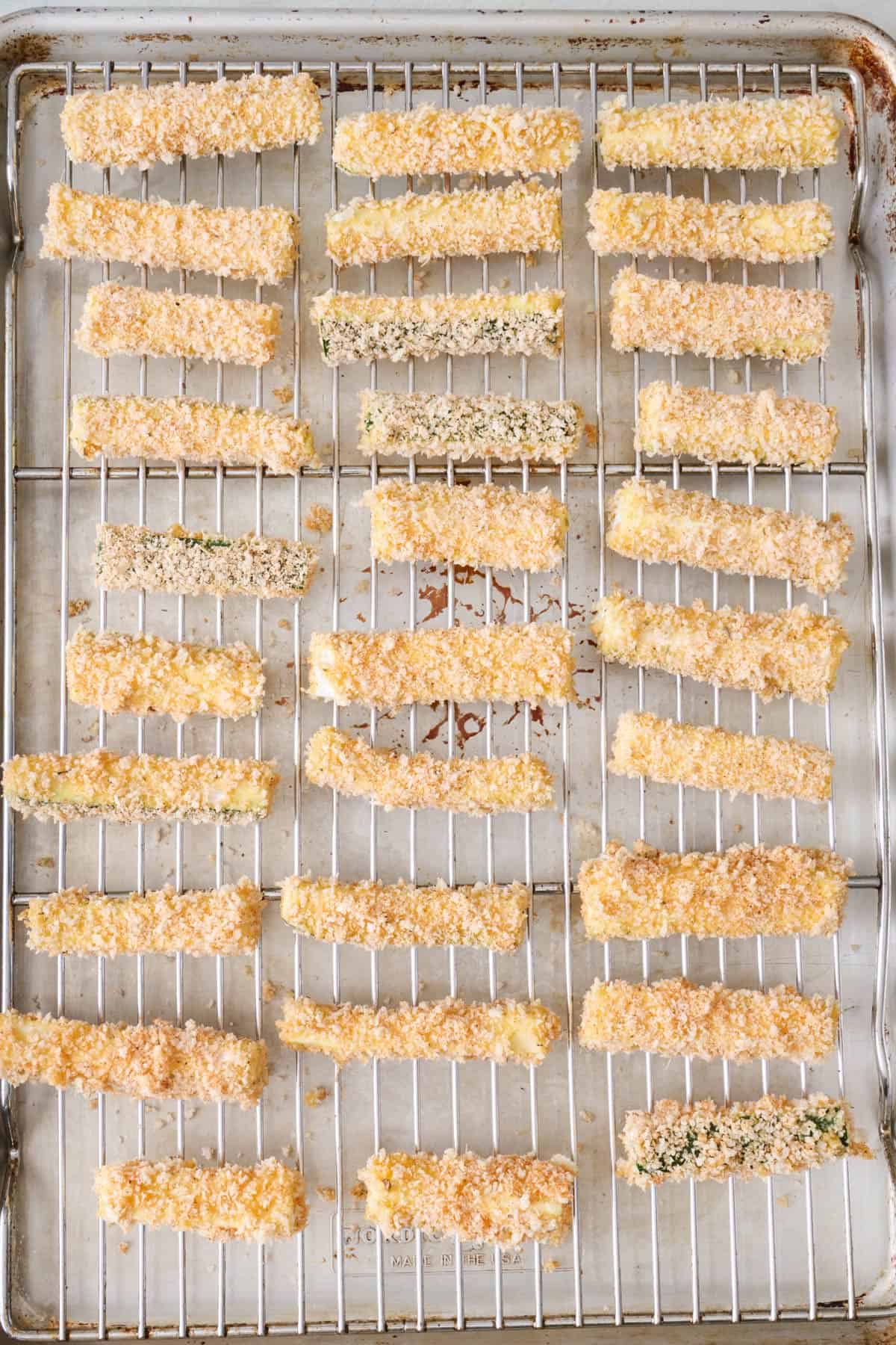 Unbaked zucchini fries on a cooling rack on a sheet pan.