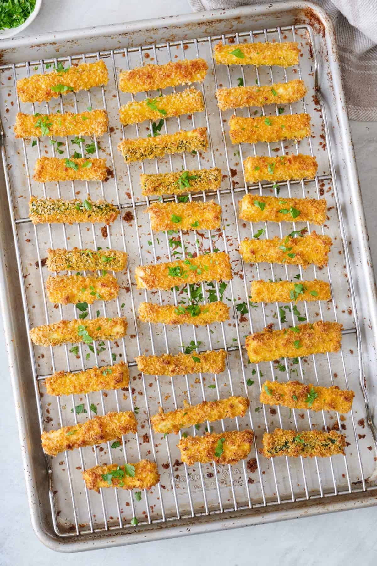 Crispy baked zucchini fries sprinkled with chopped, fresh herbs on a baking sheet.