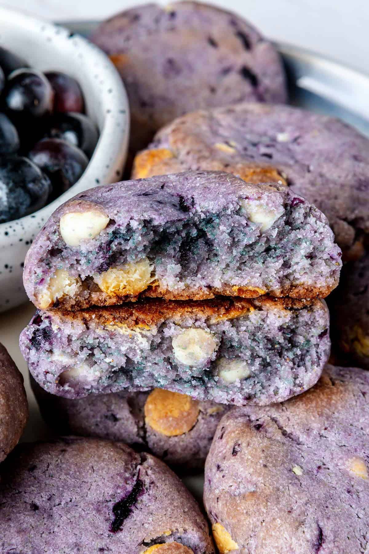 Close up on plate of blueberry and white chocolate chip cookies with one cookie broken in half to show inside texture.