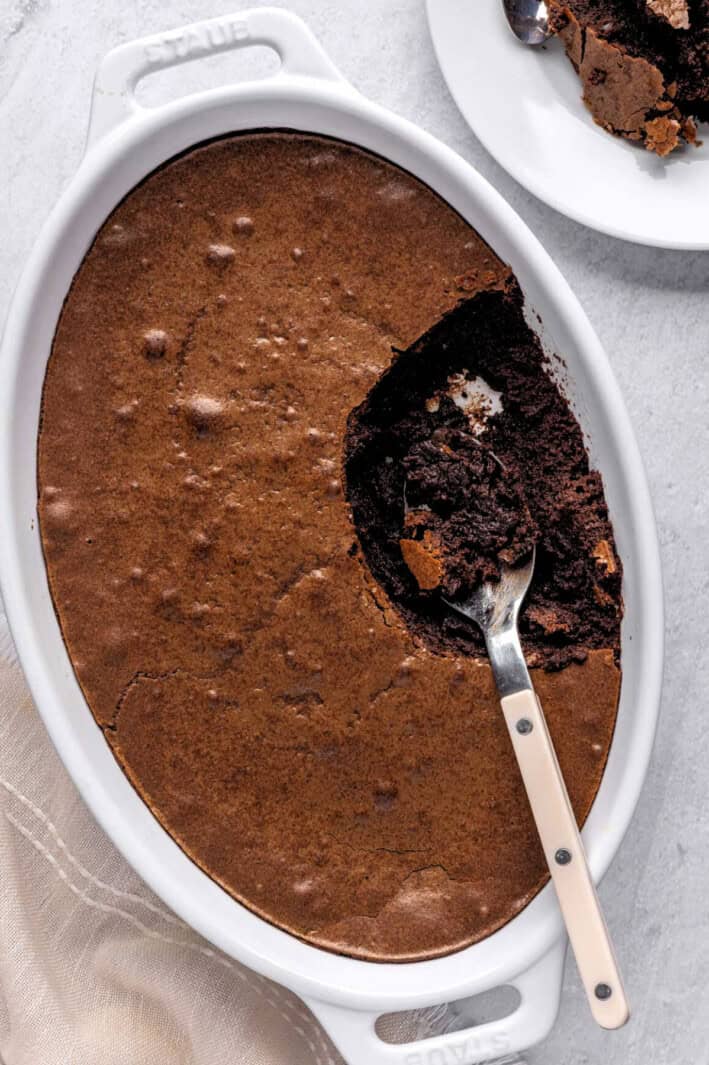 Homemade brownie pudding recipe in an oval baking dish with a serving removed to a small plate nearby.
