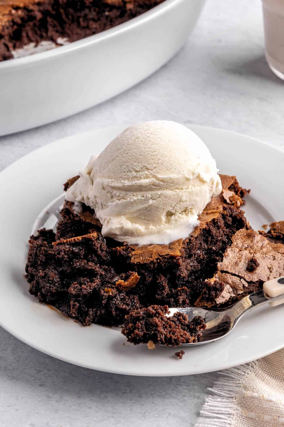 Serving of brownie pudding on a plate with a scoop of vanilla ice cream on top.