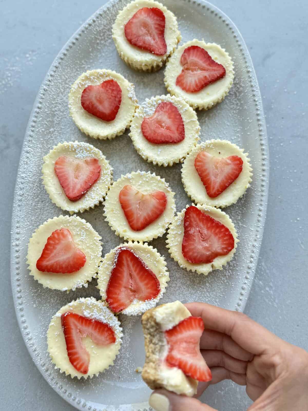 Cottage Cheesecake cups on a platter topped with strawberries with hand holding one of them bitten out of