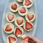 Cottage Cheesecake cups on a platter topped with strawberries with hand holding one of them bitten out of