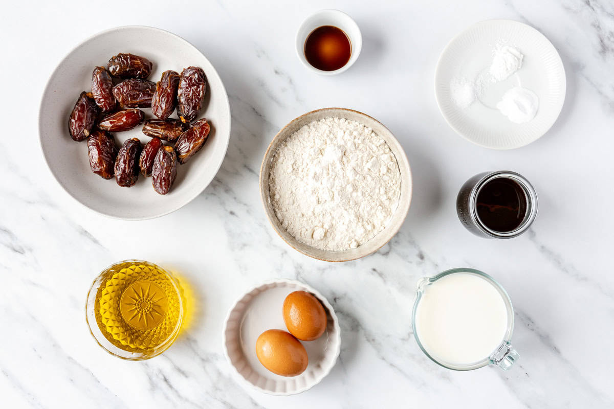 Ingredients for recipe in individual dishes: dates, vanilla, oil, eggs, flour, salt, baking powder, baking soda, milk, and date syrup.