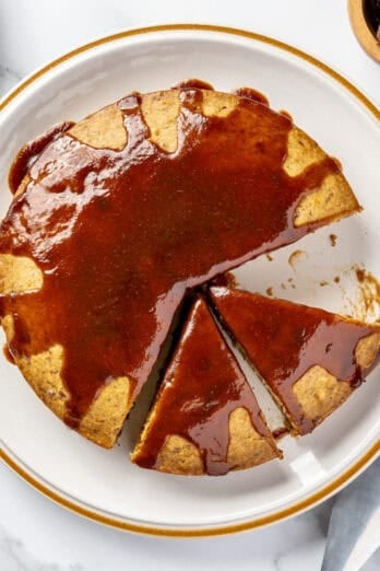 Date cake topped with date syrup on a plate with a few slices cut away.