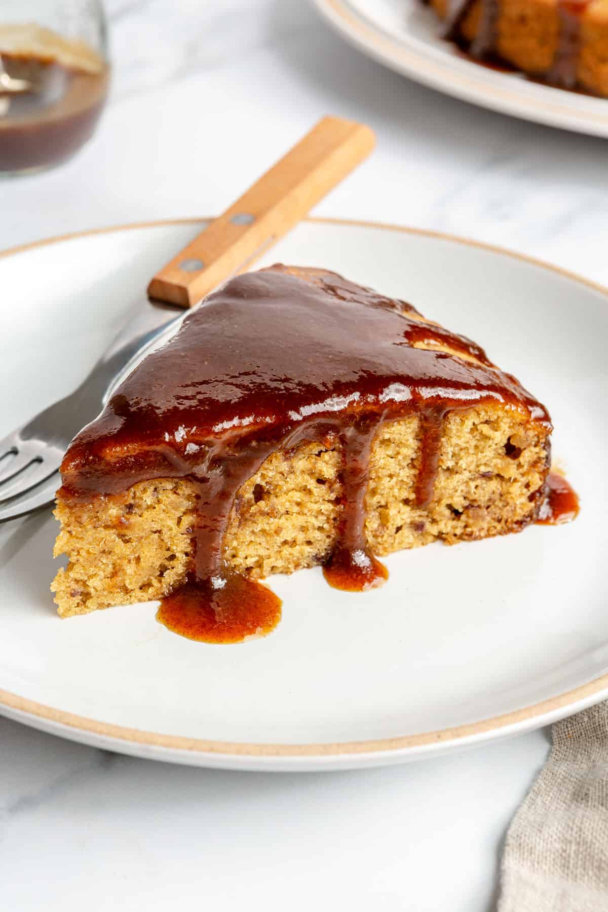 Slice of date cake on a plate covered in date syrup.