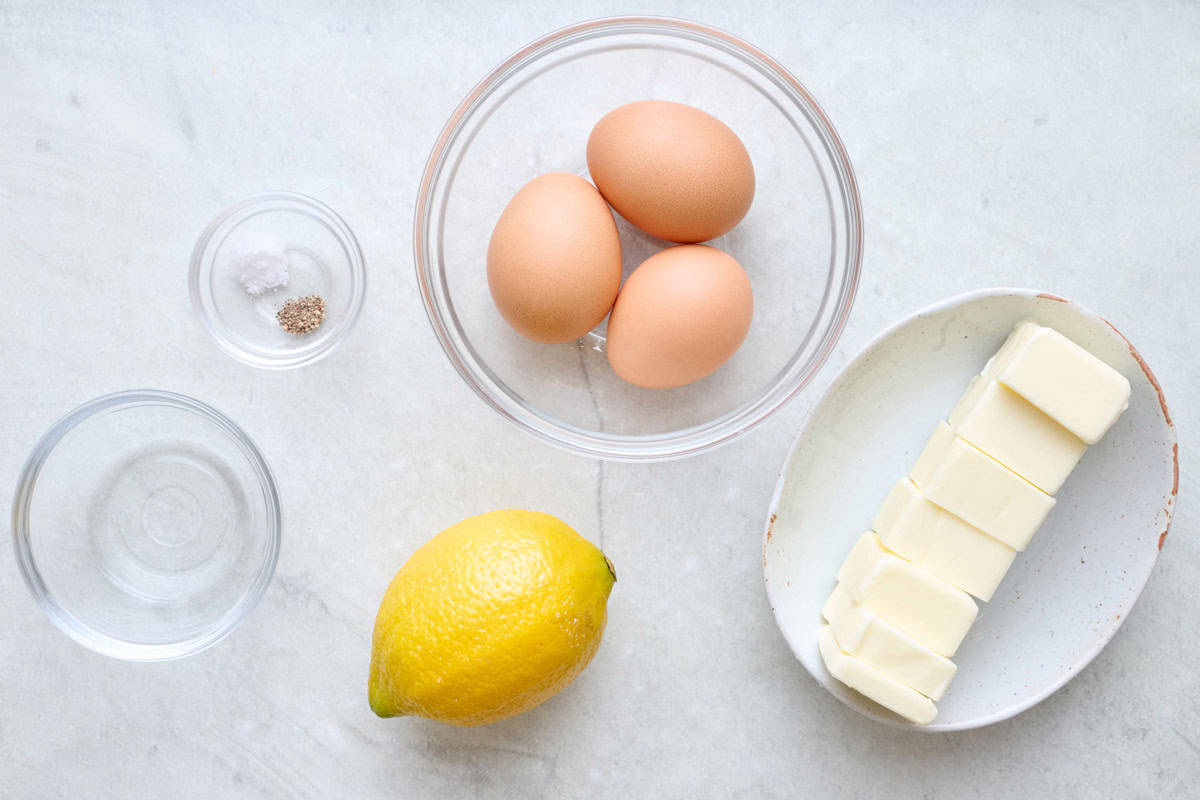 Whisking hollandaise sauce in a glass bowl over a pot of boiling water and pouring in melted butter.